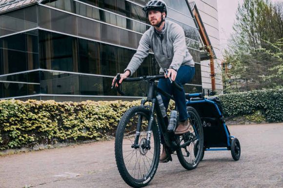 Un cycliste sur VTT avec un chariot pour faire ses courses fixé à l'arrière